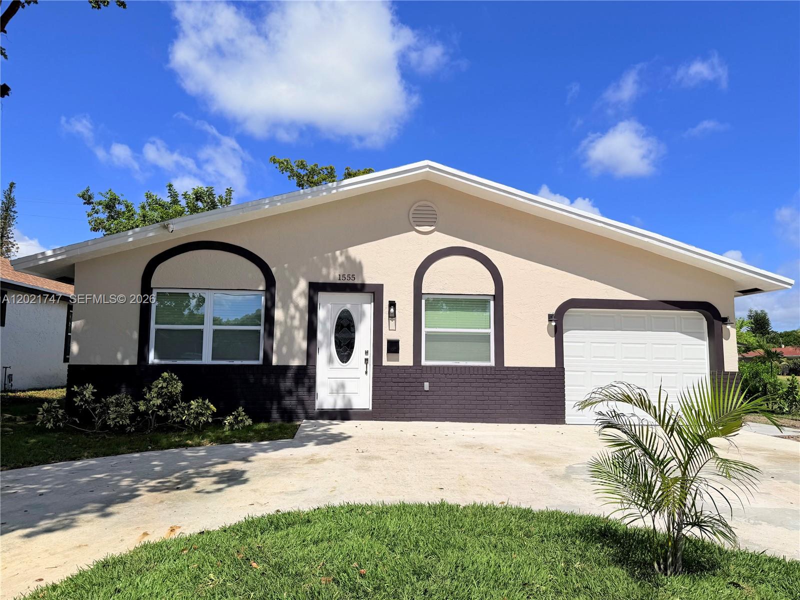 A single-story house with a beige stucco exterior, dark brick base, and a concrete driveway — 1555 NW 6th Ave, Pompano Beach FL 33060, POMPANO BEACH, FL