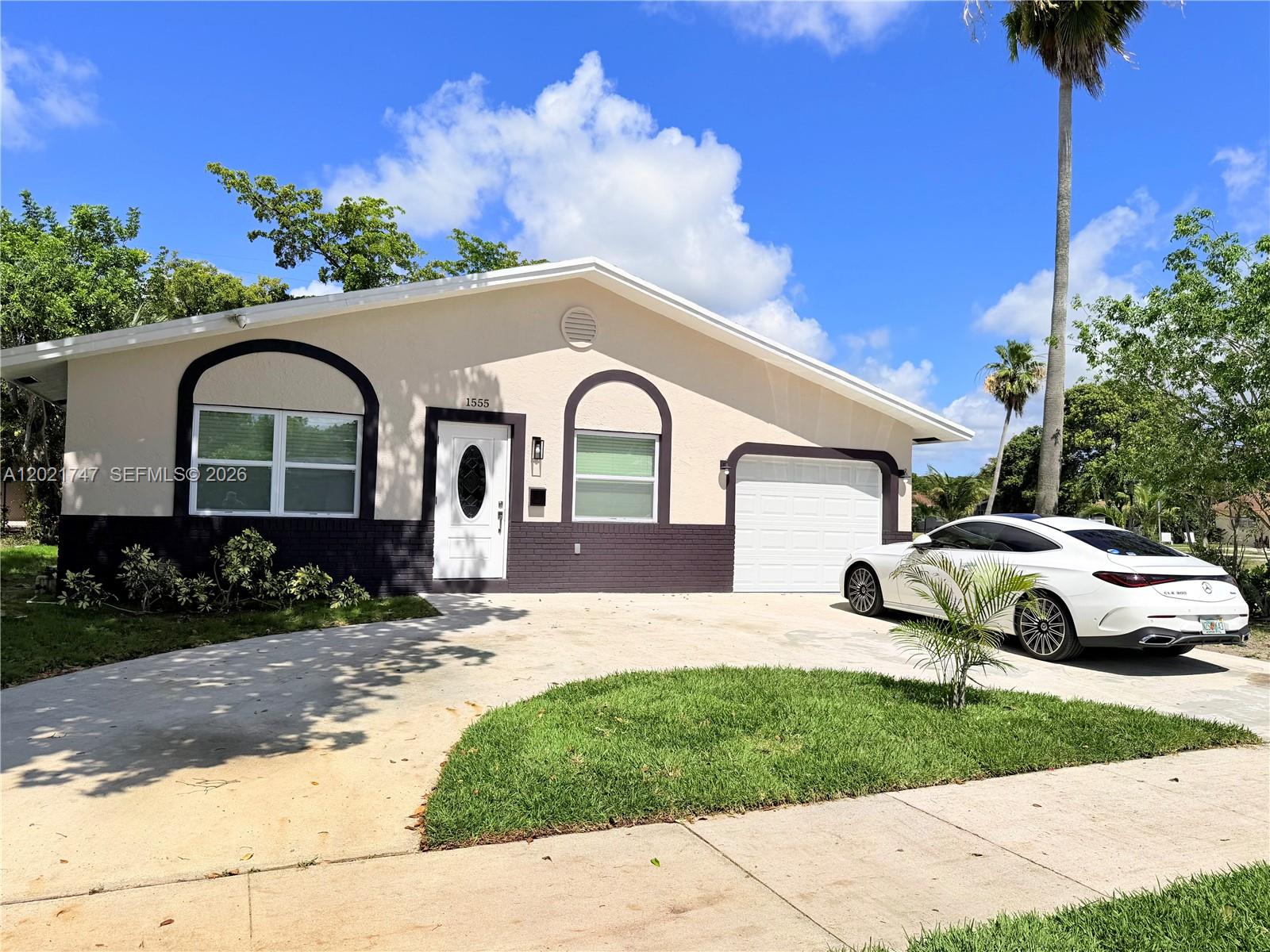 A single-story house with a white and dark brown exterior features a white garage door — 1555 NW 6th Ave, Pompano Beach FL 33060, POMPANO BEACH, FL