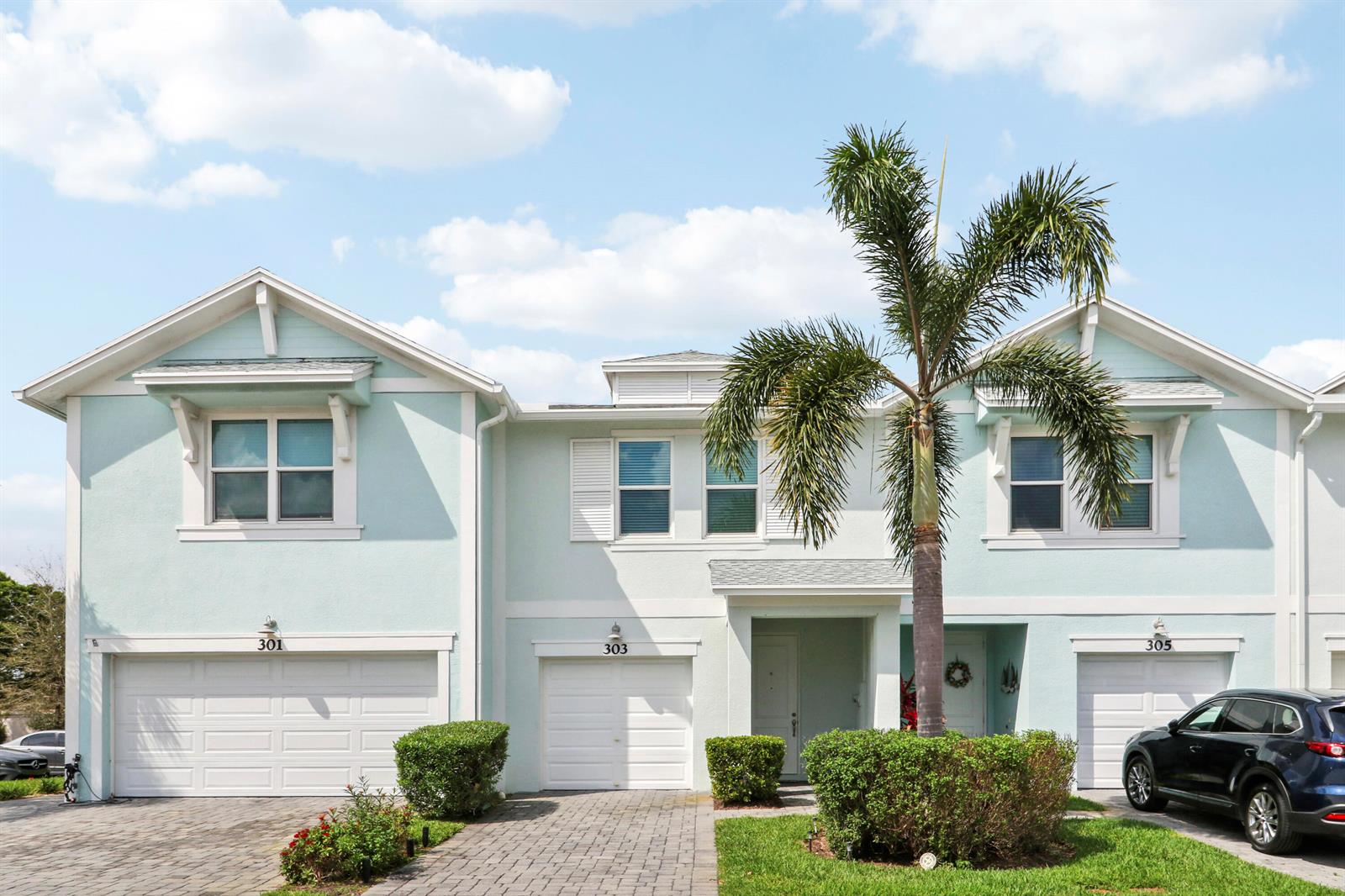 A row of three light blue townhouses with white trim, garages, and a palm tree — 303 SE Halifax Lane, Stuart FL 34994, STUART, FL