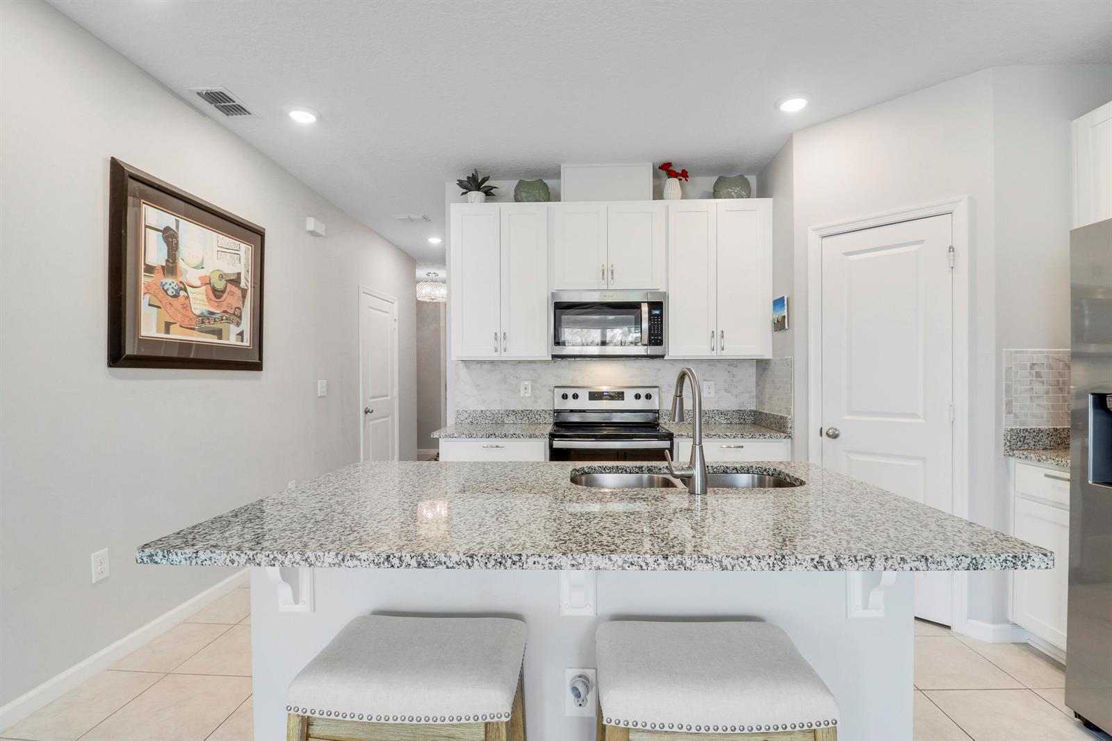 A kitchen features a granite-topped island, white cabinetry, stainless steel appliances, and two stools — 303 SE Halifax Lane, Stuart FL 34994, STUART, FL