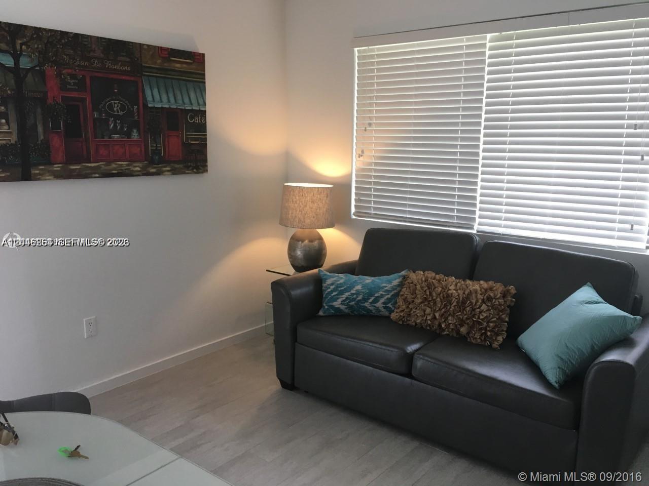 A living room features a dark gray sofa, a table lamp, and wall art — 1601 Meridian Ave # 110, Miami Beach FL 33139, MIAMI BEACH, FL