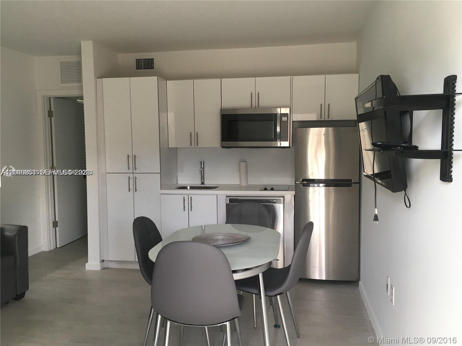 A compact kitchen features white cabinets, stainless steel appliances, and a small dining table — 1601 Meridian Ave # 110, Miami Beach FL 33139, MIAMI BEACH, FL