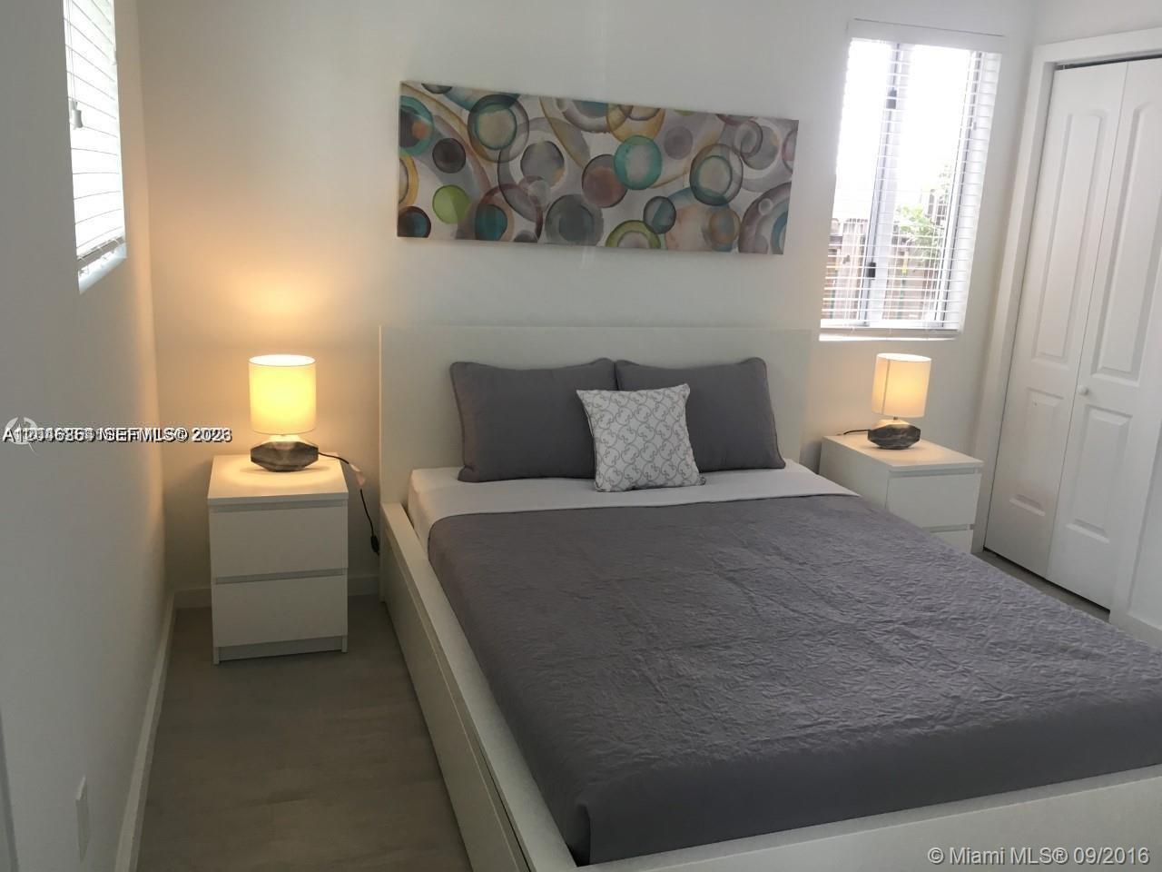 A bedroom features a bed with grey bedding, two white nightstands, and abstract wall art — 1601 Meridian Ave # 110, Miami Beach FL 33139, MIAMI BEACH, FL