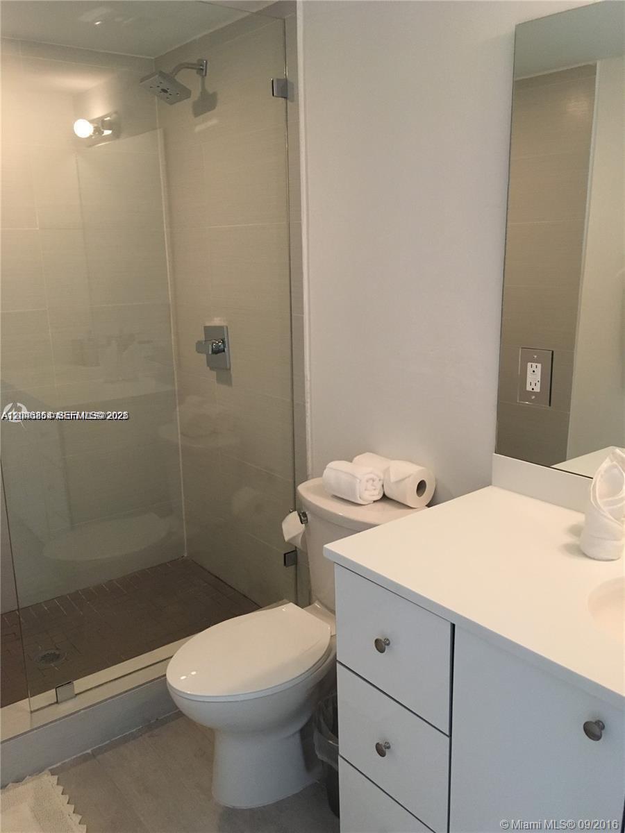 A bathroom features a glass-enclosed shower, a white vanity, and a toilet — 1601 Meridian Ave # 110, Miami Beach FL 33139, MIAMI BEACH, FL