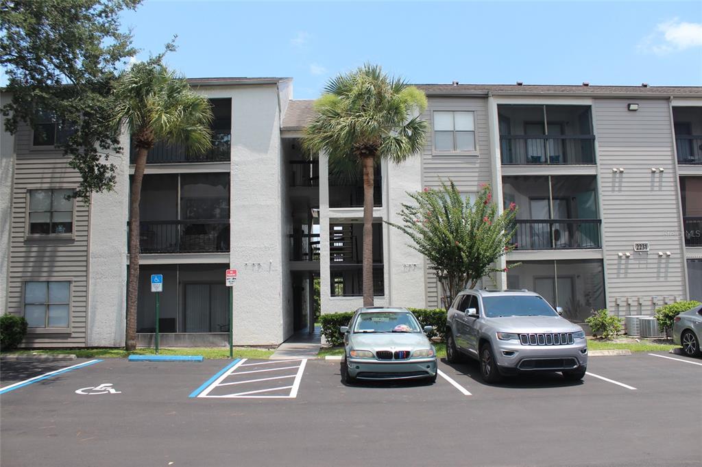 A three-story apartment building exterior with a parking lot and two palm trees in front — 2231 CASCADES BOULEVARD UNIT 304, KISSIMMEE, FL