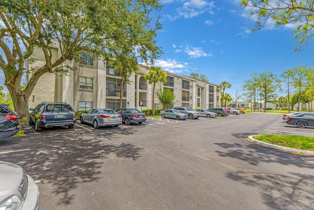 A multi-story apartment building with a parking lot in the foreground under a blue sky — 2231 CASCADES BOULEVARD UNIT 304, KISSIMMEE, FL