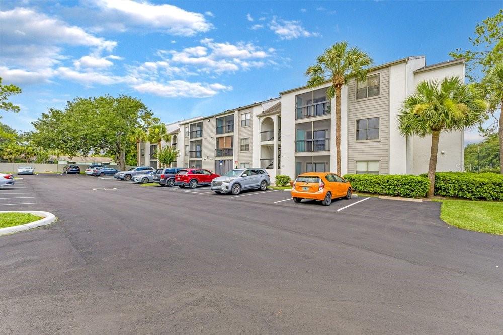 A multi-story apartment building with a parking lot in the foreground under a blue sky — 2231 CASCADES BOULEVARD UNIT 304, KISSIMMEE, FL