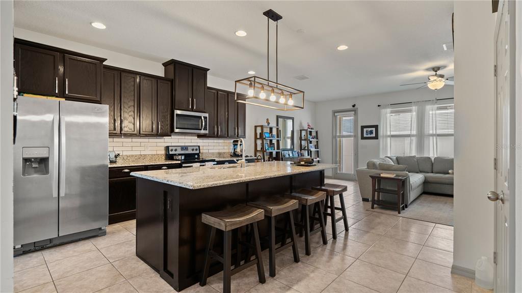 A kitchen with dark wood cabinets, granite countertops, and an island with bar stools — 8113 RED STOPPER LANE, WINTER GARDEN, FL