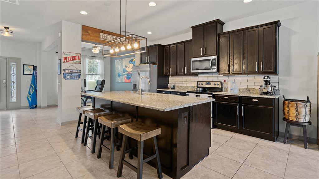 A kitchen features dark wood cabinets, granite countertops, a central island, and four bar stools — 8113 RED STOPPER LANE, WINTER GARDEN, FL