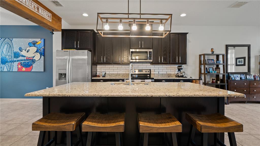 A kitchen features a granite-topped island, dark wood cabinetry, and a rectangular pendant light fixture — 8113 RED STOPPER LANE, WINTER GARDEN, FL