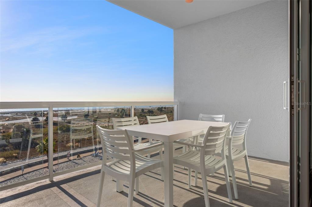 A white dining set sits on a balcony overlooking a beach and coastal landscape — 11500 GULF BOULEVARD UNIT 504, TREASURE ISLAND, FL