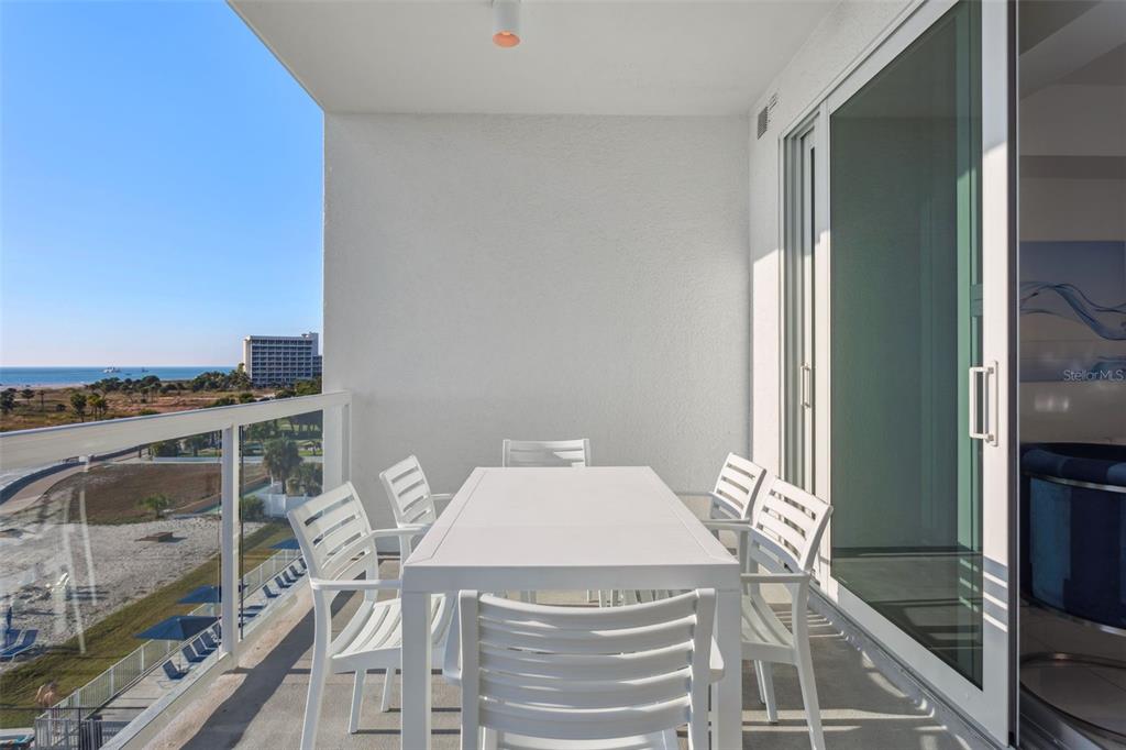 A balcony with a white dining set overlooks a beach and ocean — 11500 GULF BOULEVARD UNIT 504, TREASURE ISLAND, FL
