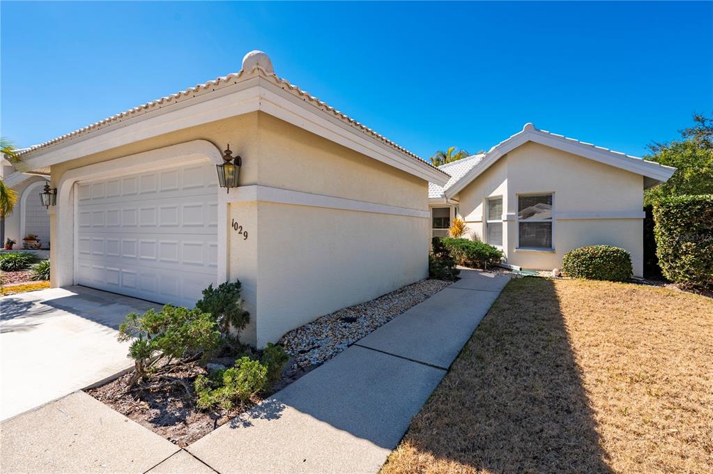 A single-story house with a white garage, beige stucco walls, and a concrete walkway — 1029 HARBOR TOWN DRIVE, VENICE, FL