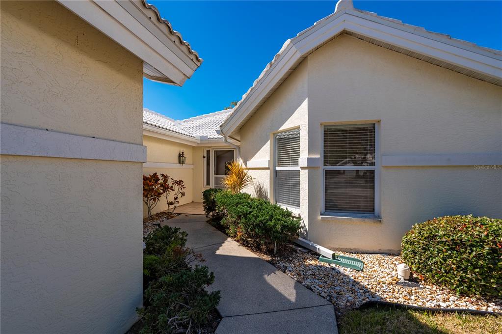 A concrete walkway leads to the front entrance of a beige house with white trim — 1029 HARBOR TOWN DRIVE, VENICE, FL