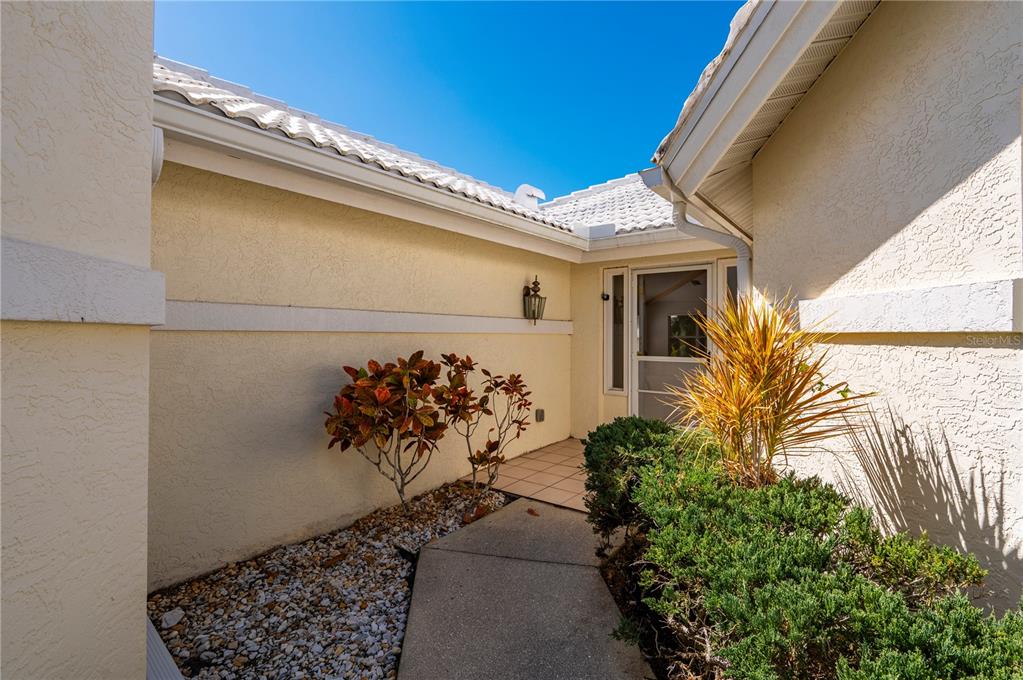 A concrete walkway leads to the front entrance of a house with light-colored stucco walls — 1029 HARBOR TOWN DRIVE, VENICE, FL