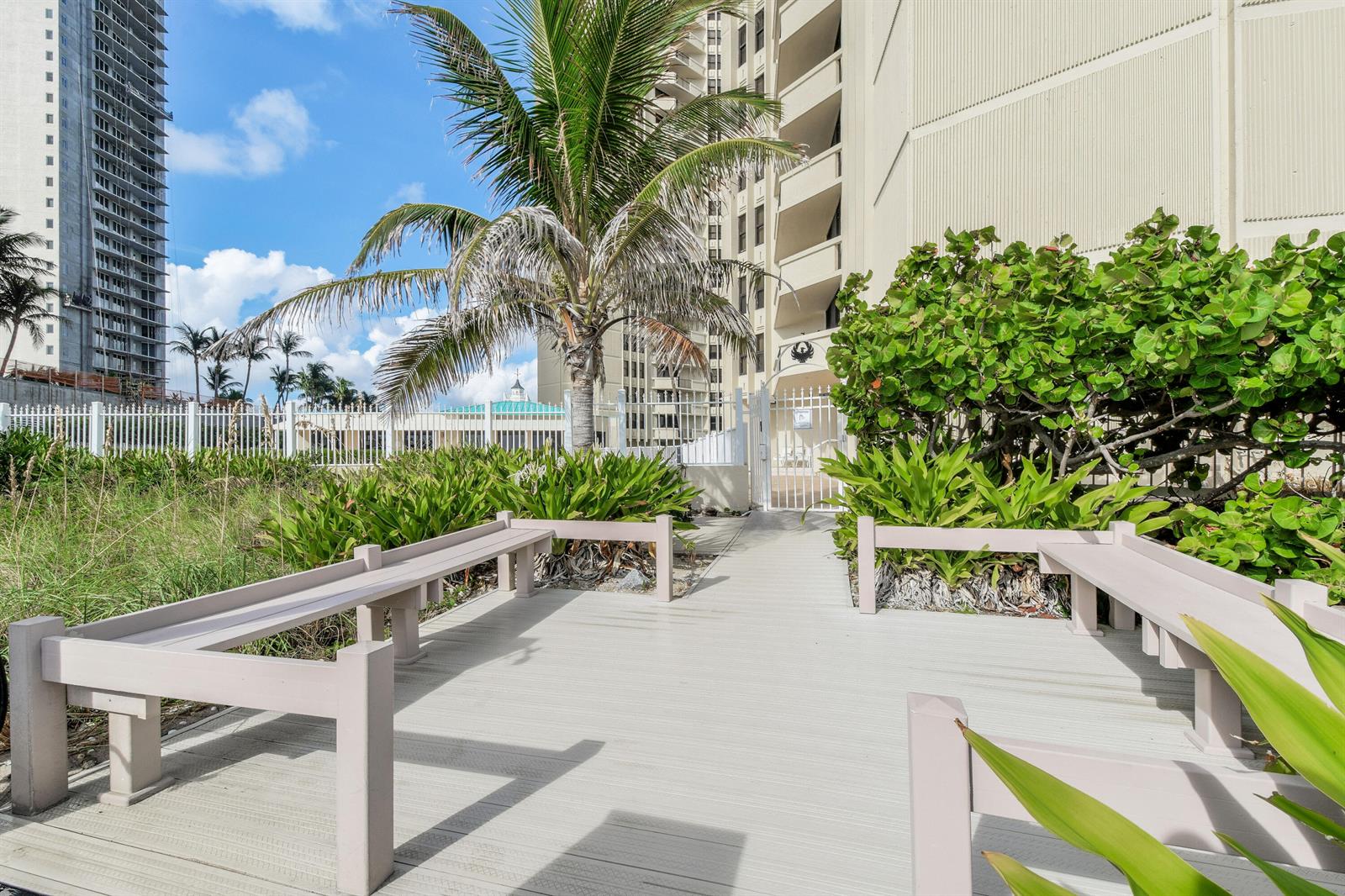 A wooden deck with built-in benches leads to a gated entrance near a palm tree — 2800 N Ocean Drive # 8b, Singer Island FL 33404, SINGER ISLAND, FL
