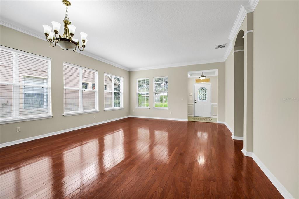 An empty room with hardwood floors, a chandelier, and multiple windows looking toward an entryway — 12718 BIDEFORD AVENUE, WINDERMERE, FL