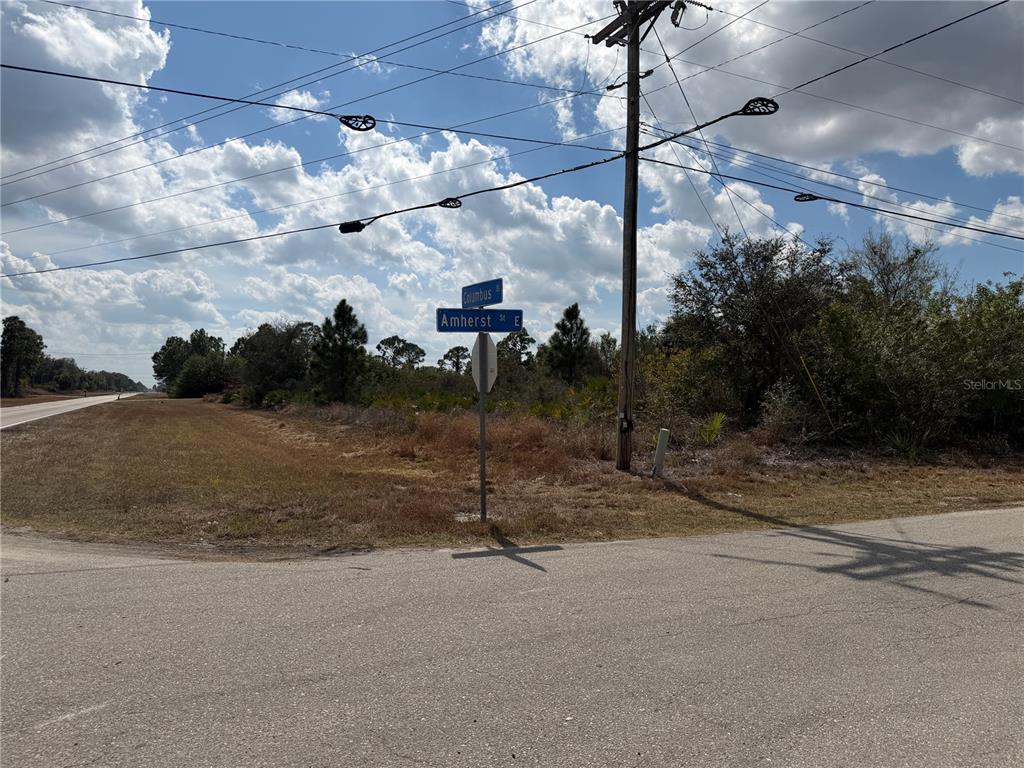 A street sign at the intersection of Columbus and Amherst Street E stands near brush — 522 COLUMBUS BOULEVARD S, LEHIGH ACRES, FL