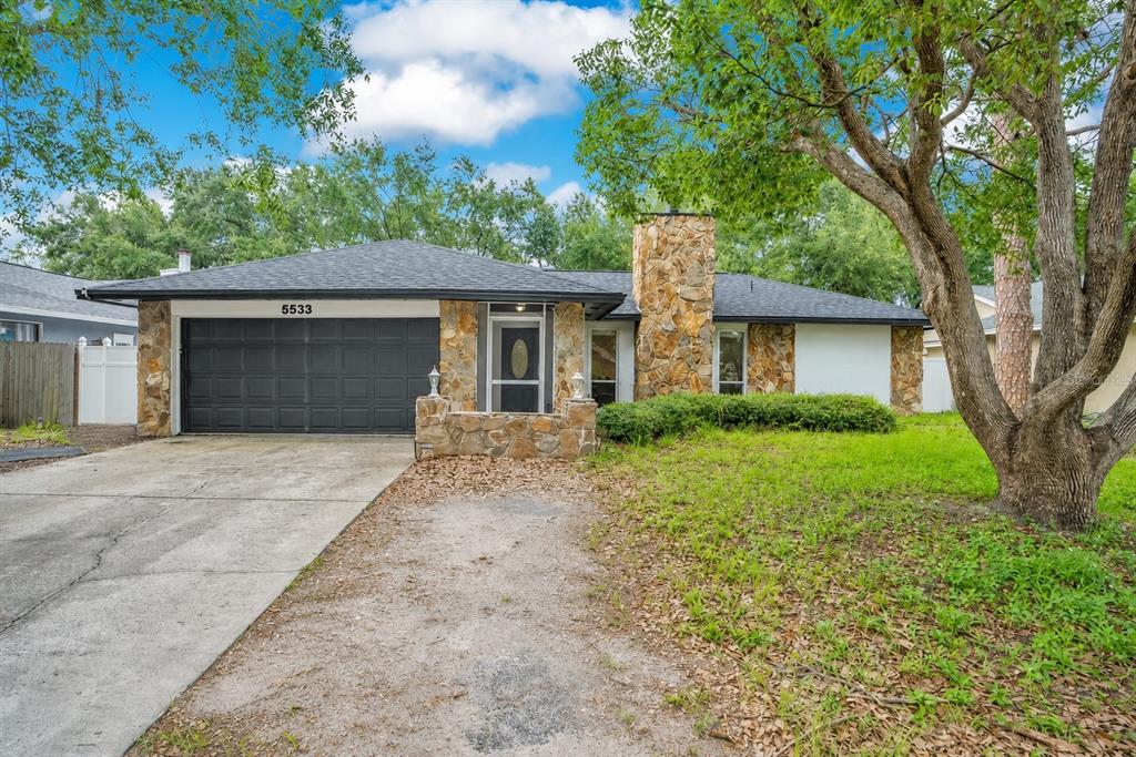 A single-story house features a stone facade, a black garage door, and a shingled roof — 5533 PENTAIL CIRCLE, TAMPA, FL