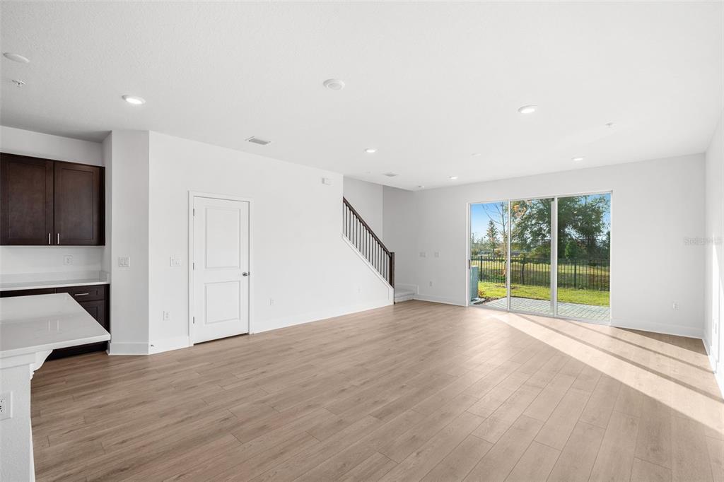 A bright living area features light wood floors, a staircase, and sliding glass doors — 1117 ORANGE TRAILSIDE WAY, OCOEE, FL