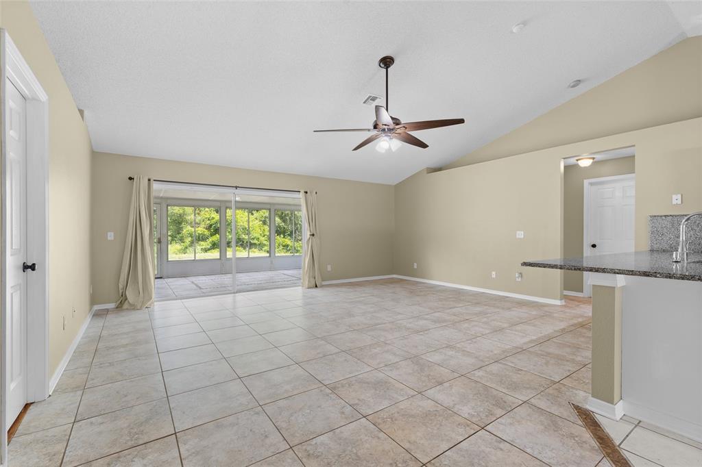 An open living area with beige walls, tile flooring, a ceiling fan, and sliding glass doors — 148 COUNTRY LAKES CIRCLE, GROVELAND, FL