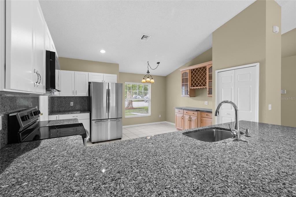 A kitchen with white cabinets, granite countertops, stainless steel appliances, and a dining area — 148 COUNTRY LAKES CIRCLE, GROVELAND, FL