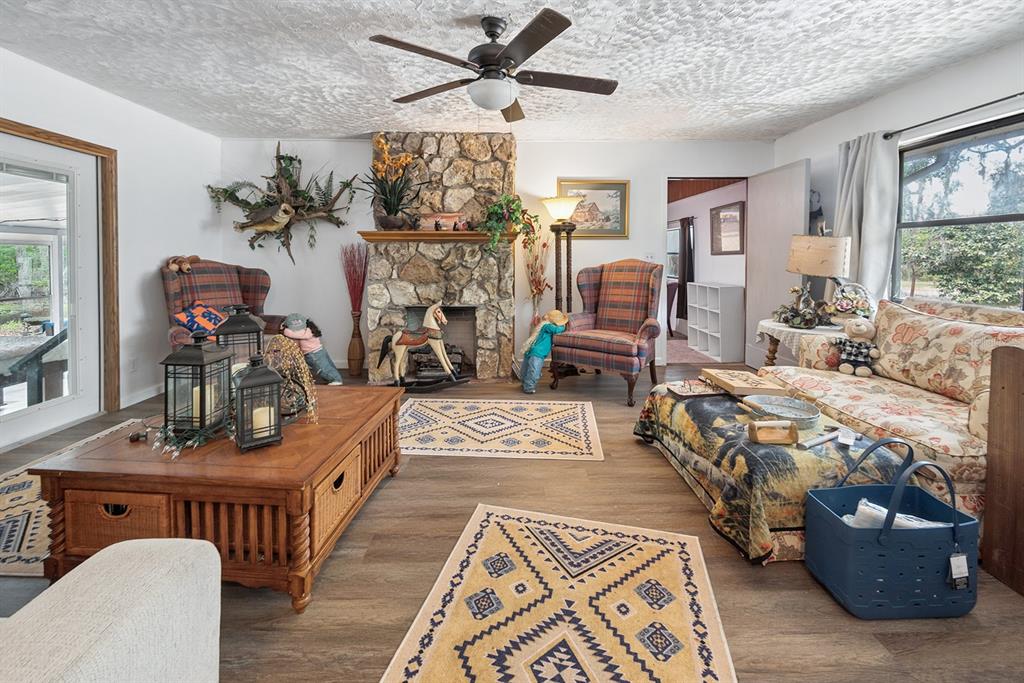 A living room features a stone fireplace, wood-look flooring, and a ceiling fan — 6308 ISLAND ROAD, MELROSE, FL