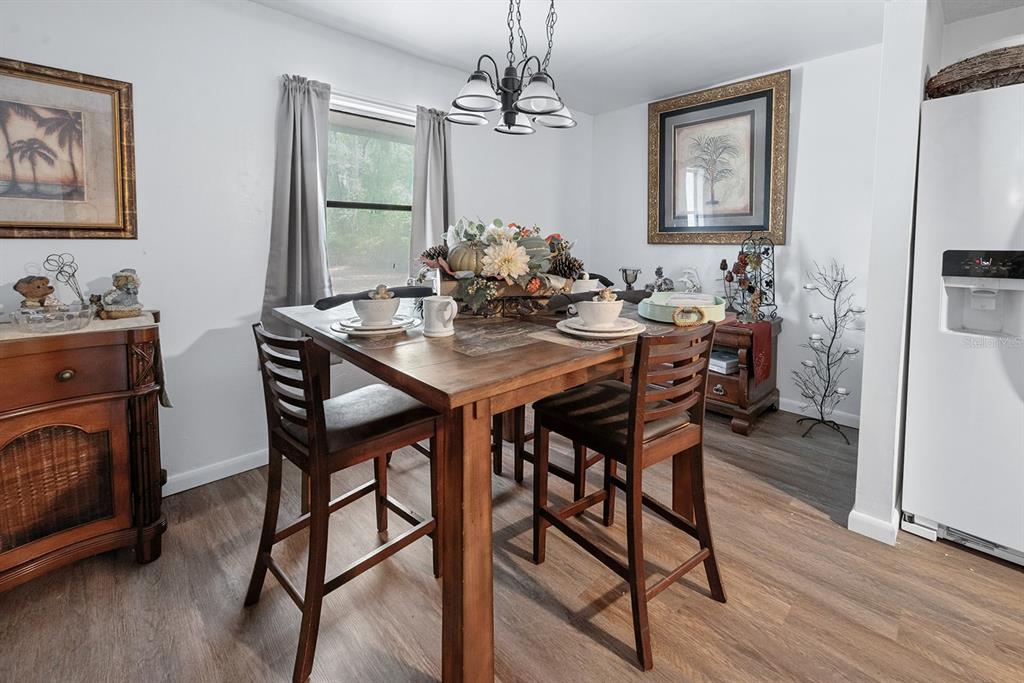 A dining area features a wooden table with four chairs, a chandelier, and wood-look flooring — 6308 ISLAND ROAD, MELROSE, FL