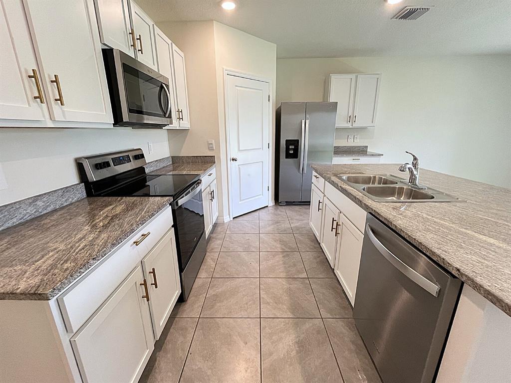 A kitchen features white cabinets, granite countertops, stainless steel appliances, and tile flooring — 12724 LATERAL ROOT DRIVE, SARASOTA, FL