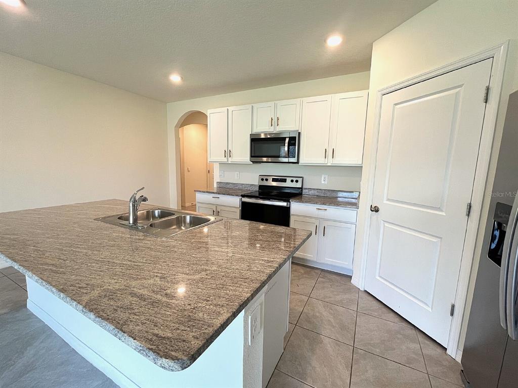 A kitchen features white cabinets, granite countertops, a large island, and tile flooring — 12724 LATERAL ROOT DRIVE, SARASOTA, FL