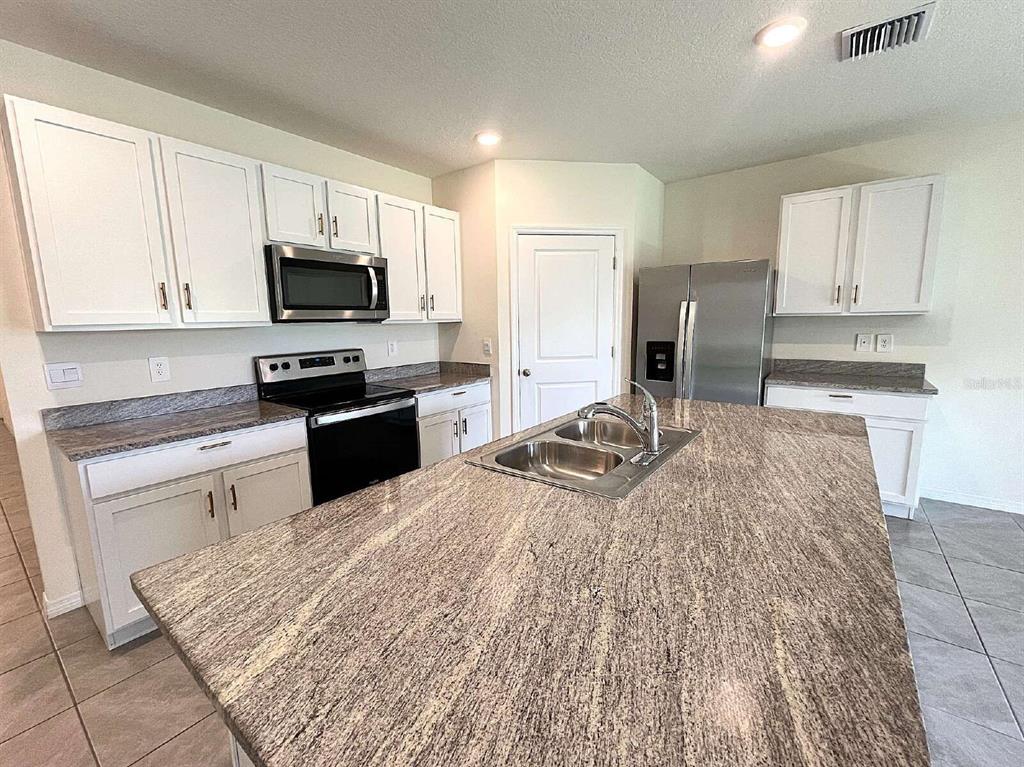 A kitchen features white cabinets, granite countertops, stainless steel appliances, and a central island — 12724 LATERAL ROOT DRIVE, SARASOTA, FL