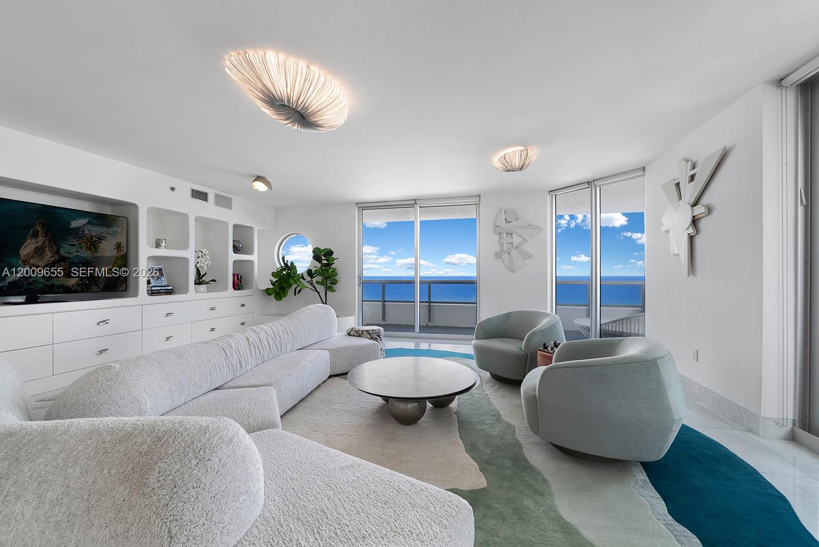 A modern living room features a white sectional, circular coffee table, and ocean views — 5801 Collins Ave # 1200, Miami Beach FL 33140, MIAMI BEACH, FL