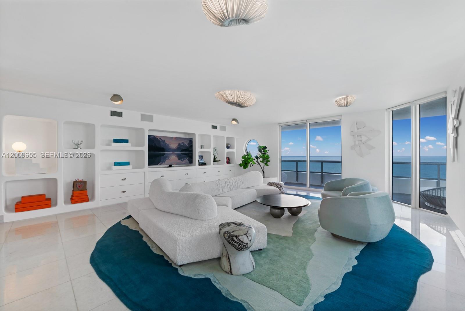 A bright living room features a white sectional, blue area rug, and ocean views — 5801 Collins Ave # 1200, Miami Beach FL 33140, MIAMI BEACH, FL