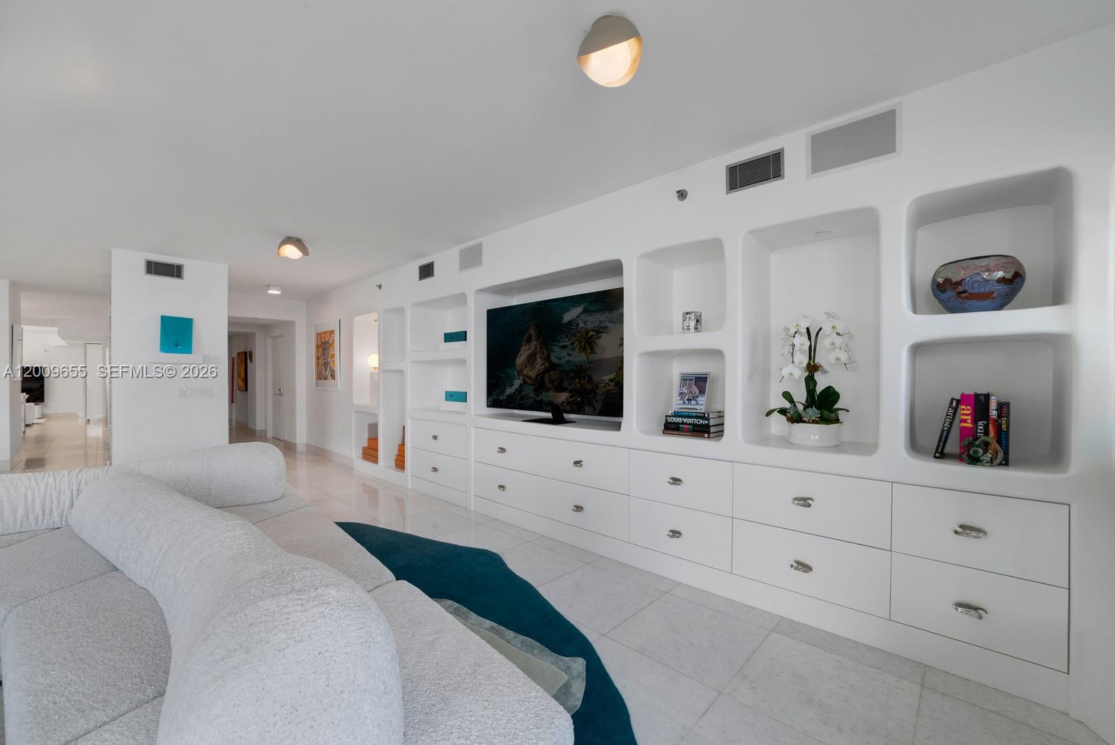 A living room features a large white built-in media wall with shelving and storage drawers — 5801 Collins Ave # 1200, Miami Beach FL 33140, MIAMI BEACH, FL