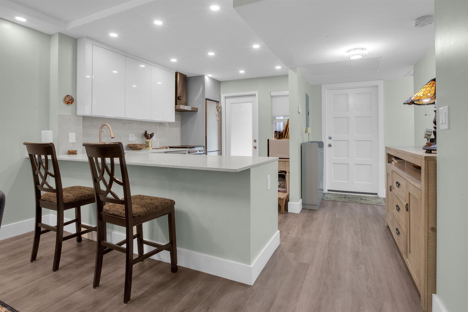 A kitchen with a breakfast bar, white cabinets, and light wood flooring near an entryway — 2600 S Course Drive # 106, Pompano Beach FL 33069, POMPANO BEACH, FL