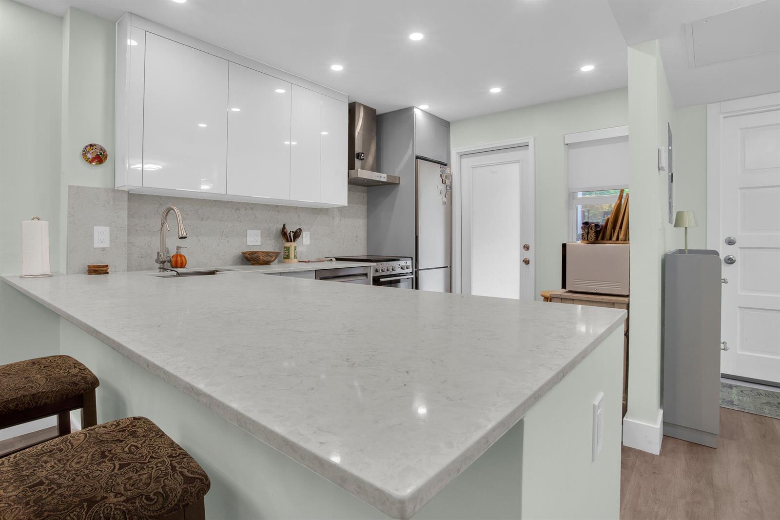 A modern kitchen features white glossy cabinets, a quartz countertop island, and stainless steel appliances — 2600 S Course Drive # 106, Pompano Beach FL 33069, POMPANO BEACH, FL