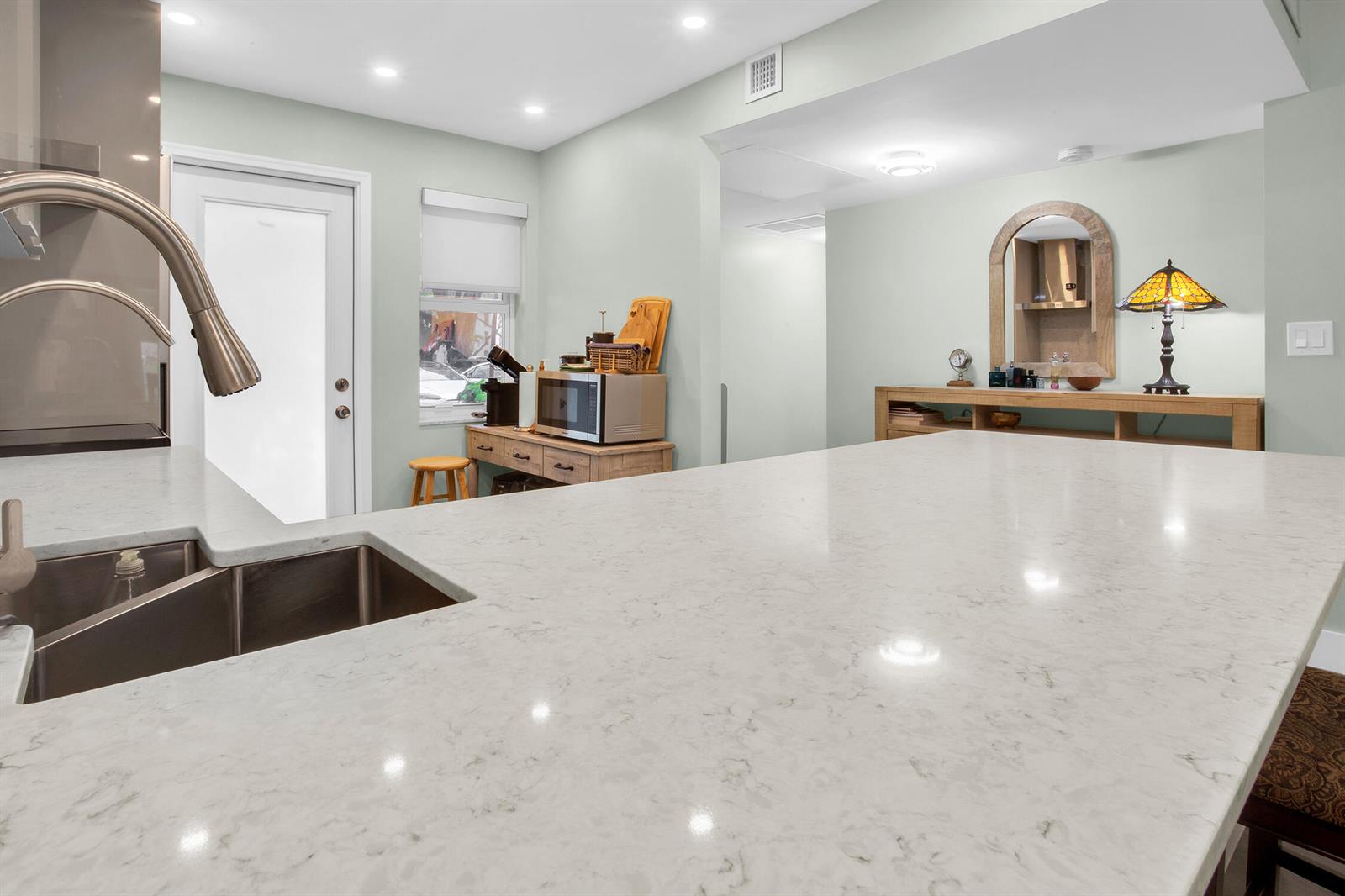 A kitchen featuring a large white quartz island, stainless steel sink, and light green walls — 2600 S Course Drive # 106, Pompano Beach FL 33069, POMPANO BEACH, FL