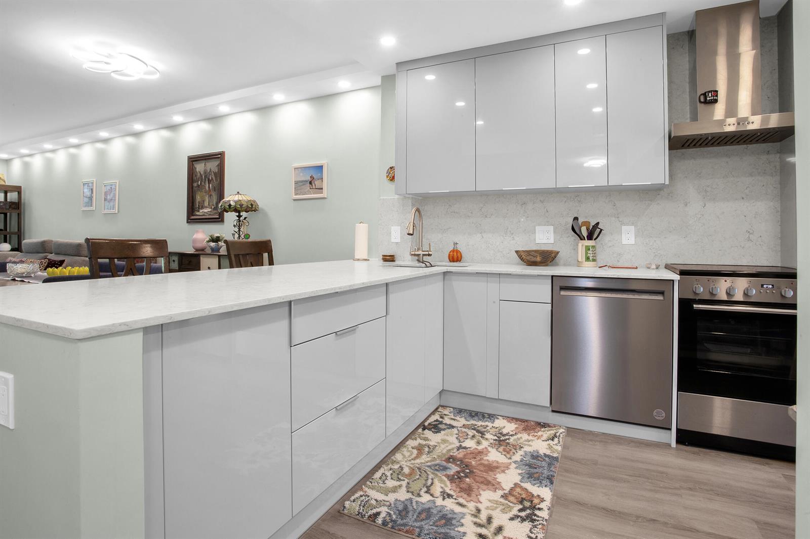 A modern kitchen features light gray glossy cabinets, white quartz countertops, and stainless steel appliances — 2600 S Course Drive # 106, Pompano Beach FL 33069, POMPANO BEACH, FL