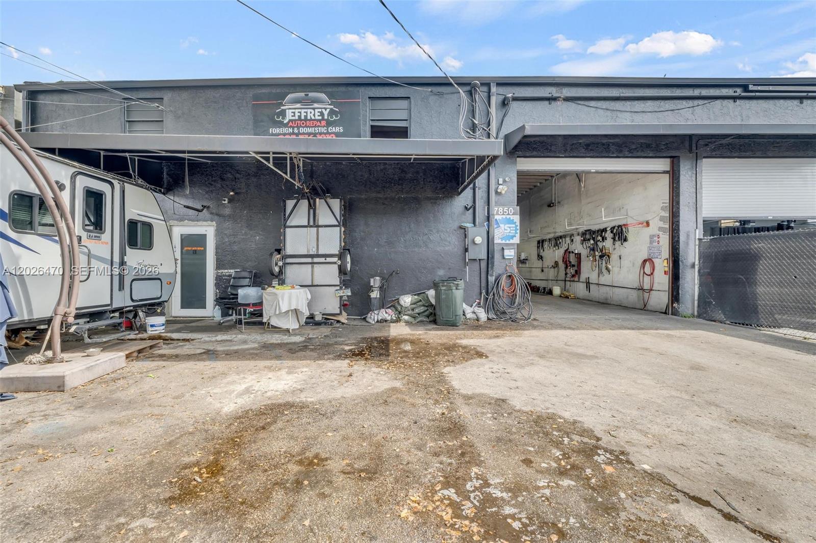 The exterior of an auto repair shop features a dark facade, a trailer, and an open bay — 7850 NW 56th St, Doral FL 33166, DORAL, FL
