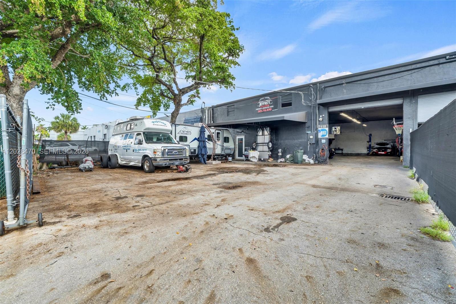 An exterior view of an auto repair shop with a gravel lot and parked vehicles — 7850 NW 56th St, Doral FL 33166, DORAL, FL