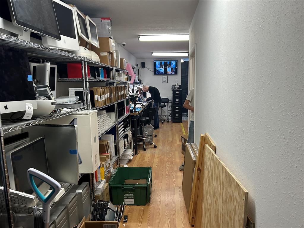 A narrow, cluttered computer repair workshop features metal shelving units, a workbench, and wood flooring — 2379 SW COLLEGE ROAD Bldg 2, OCALA, FL