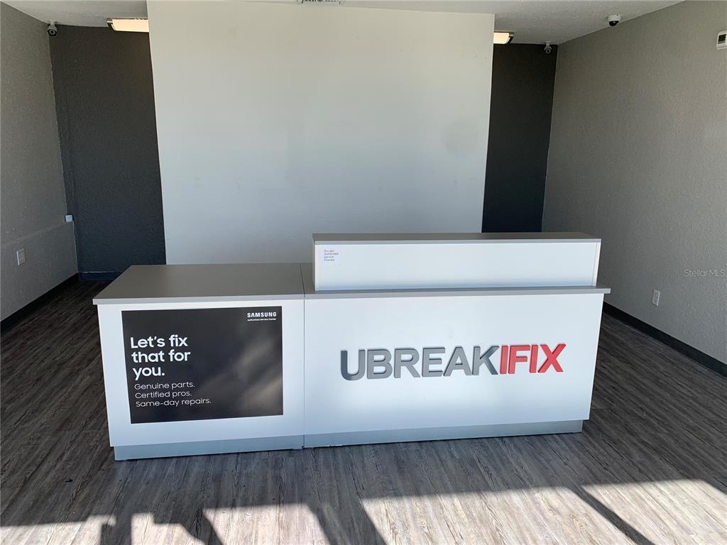 A white reception desk with UBREAKIFIX branding sits in a room with wood-look flooring — 2379 SW COLLEGE ROAD Bldg 2, OCALA, FL