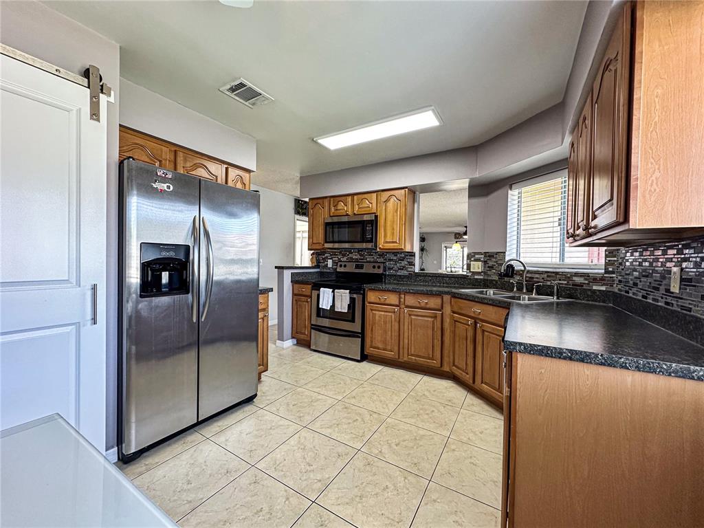 A kitchen features wood cabinets, stainless steel appliances, dark countertops, and light-colored tile flooring — 2506 TOBIN COURT, ORLANDO, FL