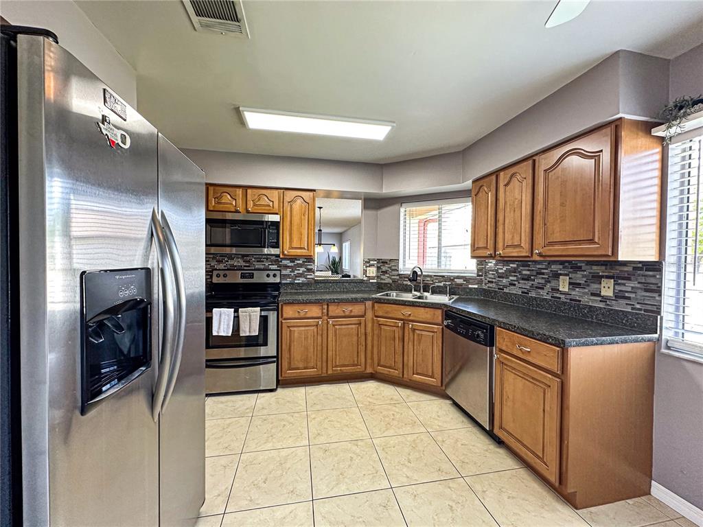 A kitchen features wood cabinets, dark countertops, stainless steel appliances, and light-colored tile flooring — 2506 TOBIN COURT, ORLANDO, FL