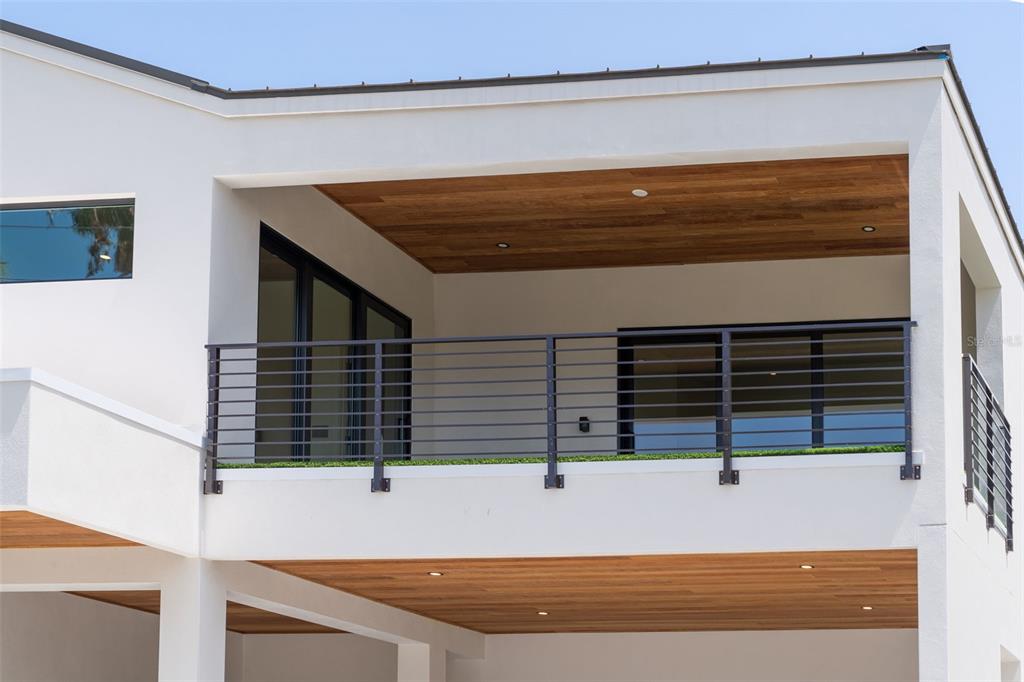 A modern house exterior features a covered balcony with wood-paneled ceilings and metal railings — 1681 OAK STREET, SARASOTA, FL