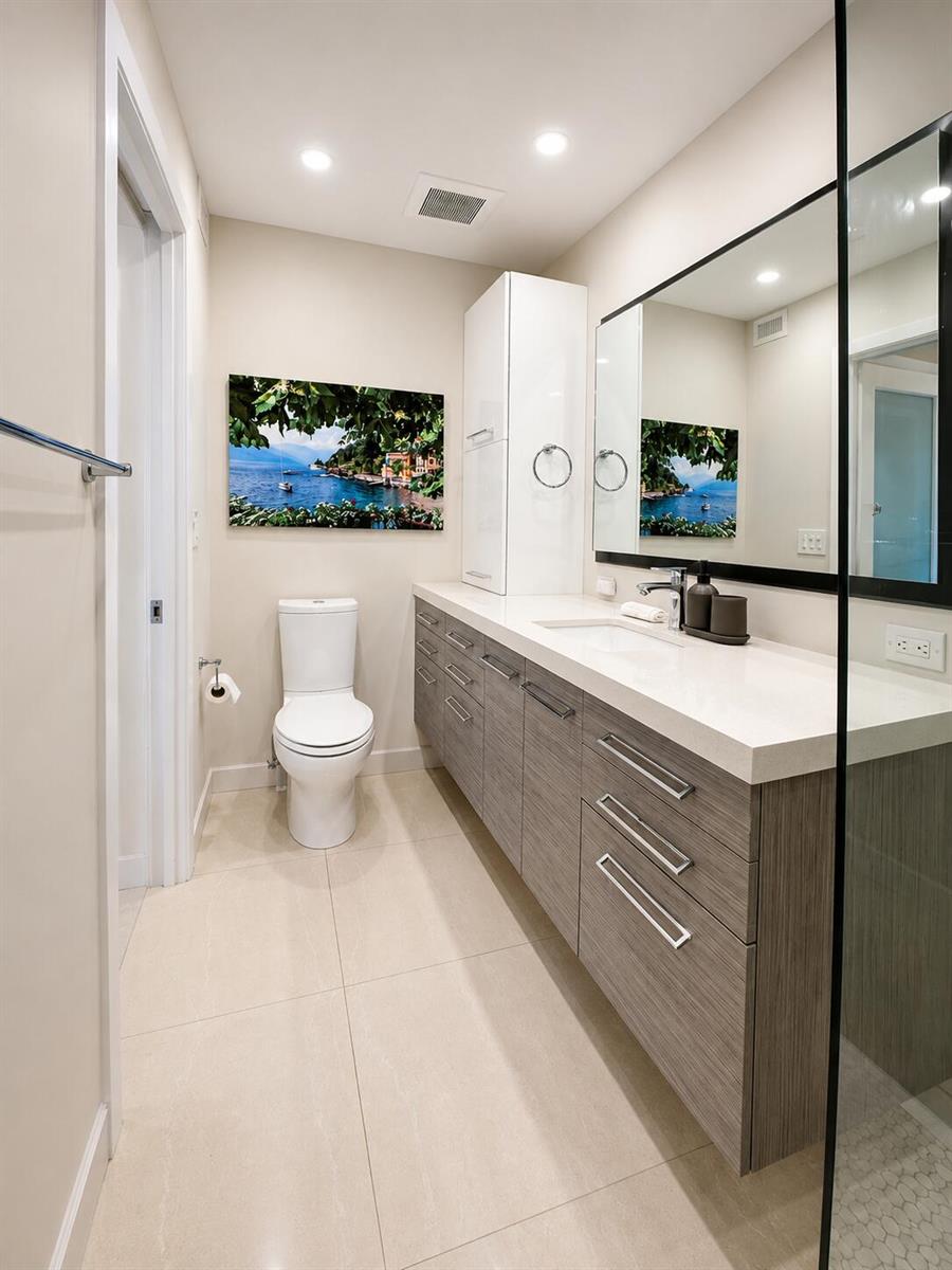 A modern bathroom features a floating wood vanity, white countertop, toilet, and a framed landscape print — 1201 S Riverside Drive # 307, Pompano Beach FL 33062, POMPANO BEACH, FL