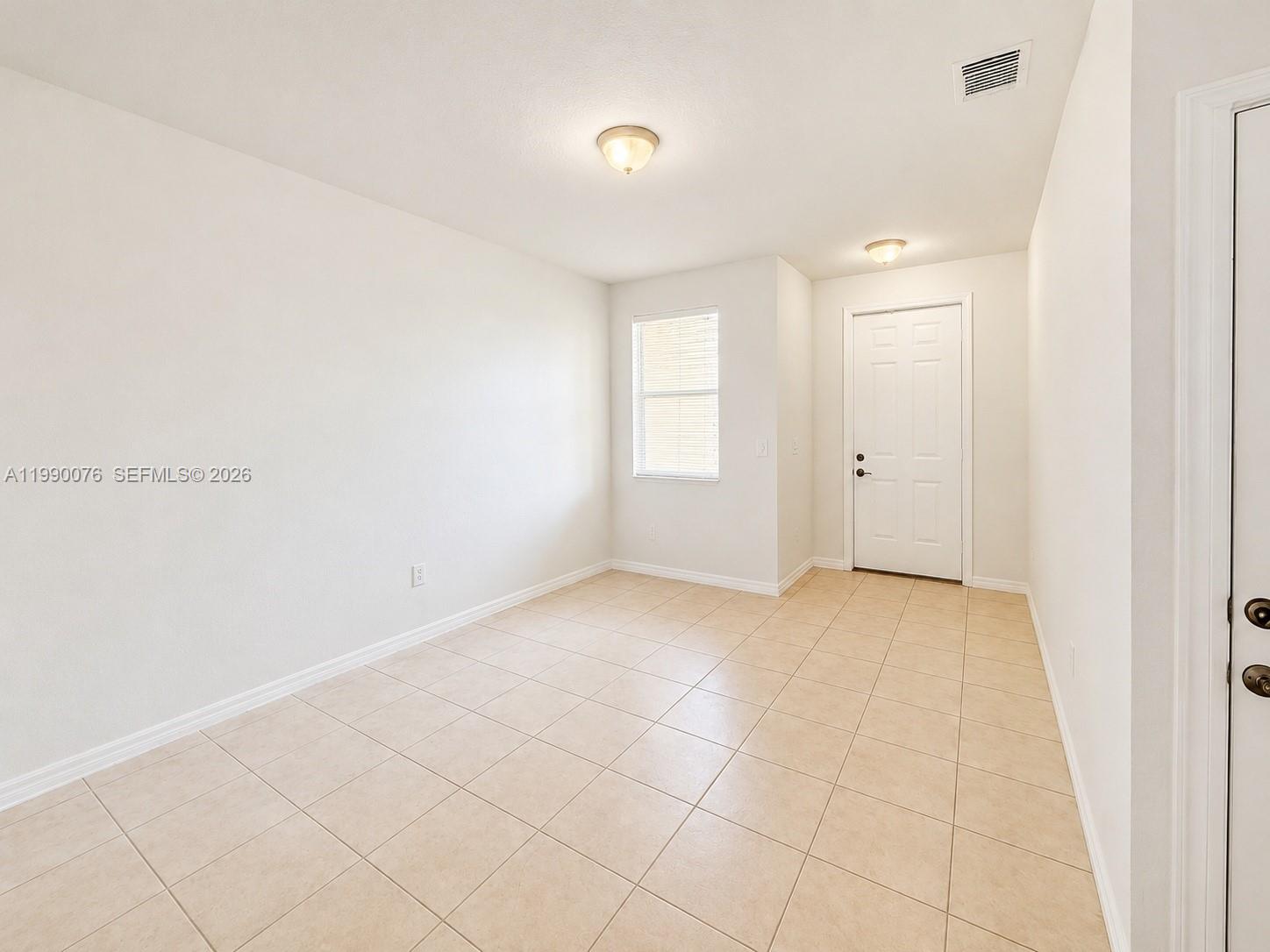 An empty room features white walls, beige tile flooring, a window, and a white door — 16649 SW 80th Ter, Miami FL 33193, MIAMI, FL