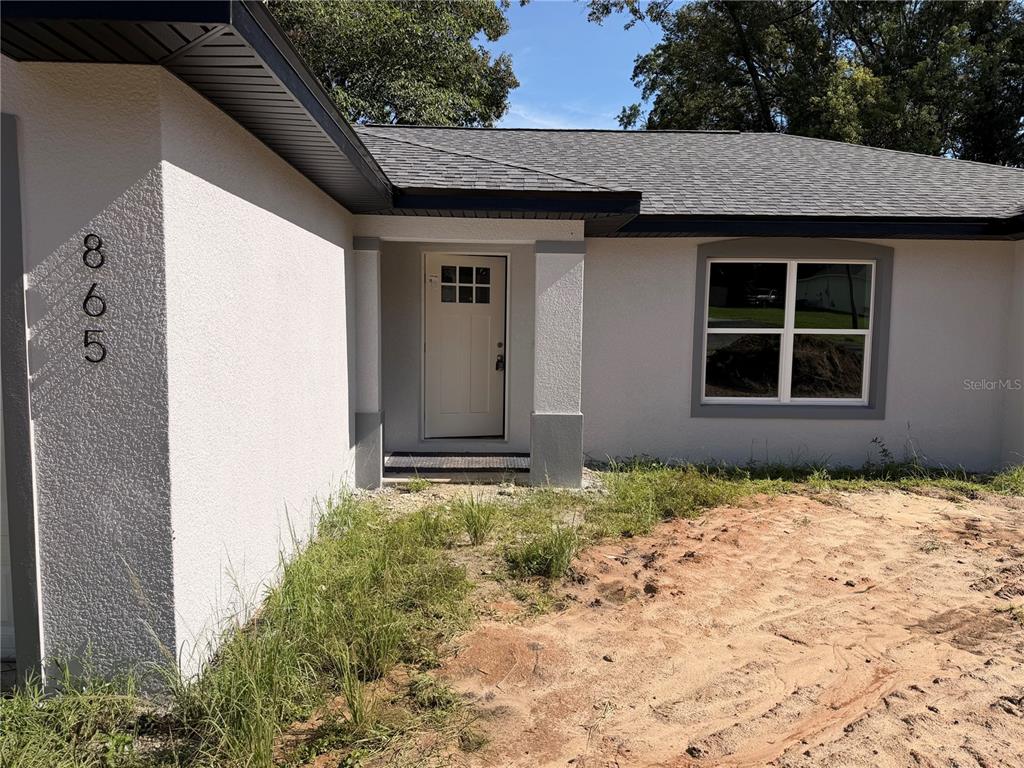 The exterior of a single-story house features a white stucco facade, a dark roof, and a front entrance — 865 SE 28TH STREET, OCALA, FL