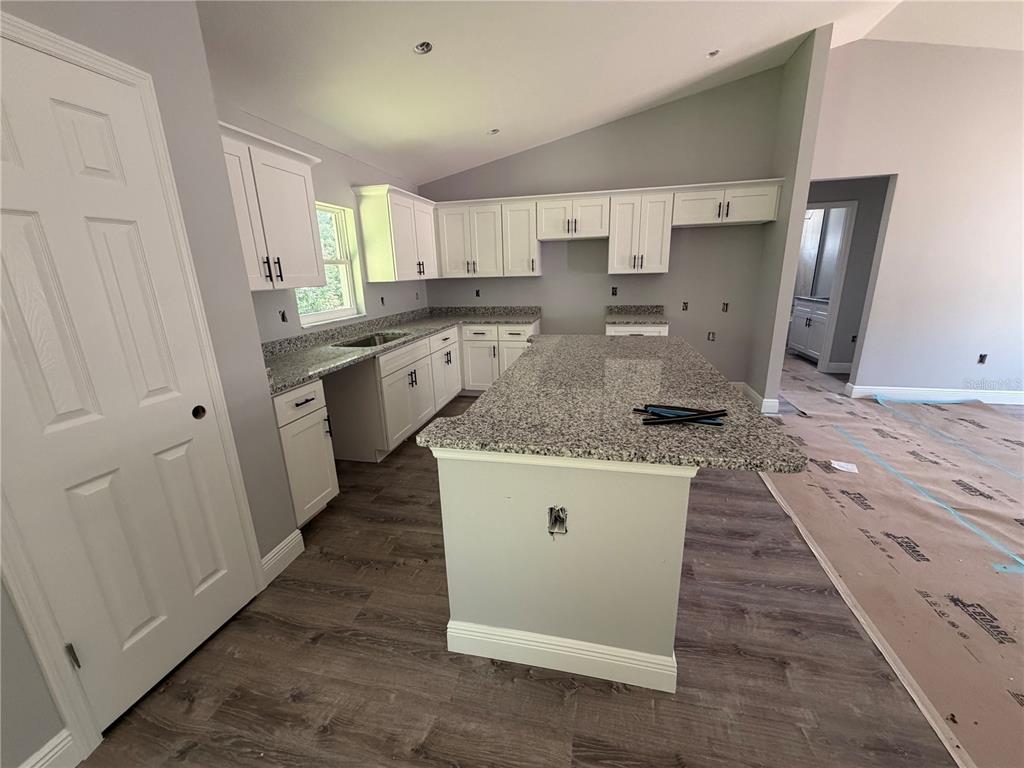 A kitchen with white cabinets, granite countertops, a central island, and wood-look flooring — 865 SE 28TH STREET, OCALA, FL