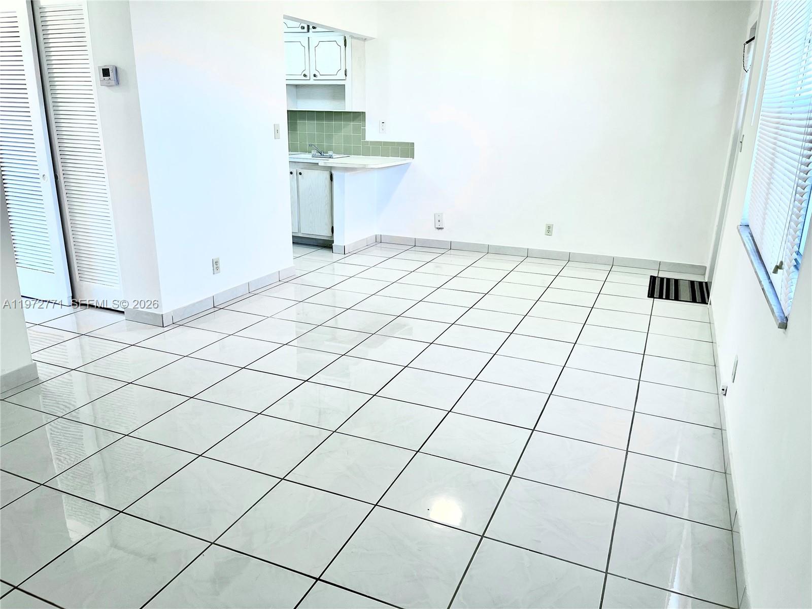 A bright, empty room features white tiled floors, white walls, and an open kitchen area — 2145 Pierce St # 421, Hollywood FL 33020, HOLLYWOOD, FL